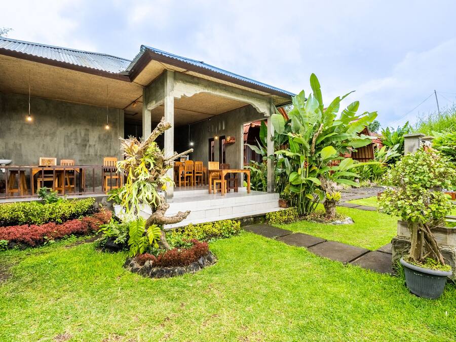 A covered outdoor seating area with tables and chairs, surrounded by lush greenery and potted plants.