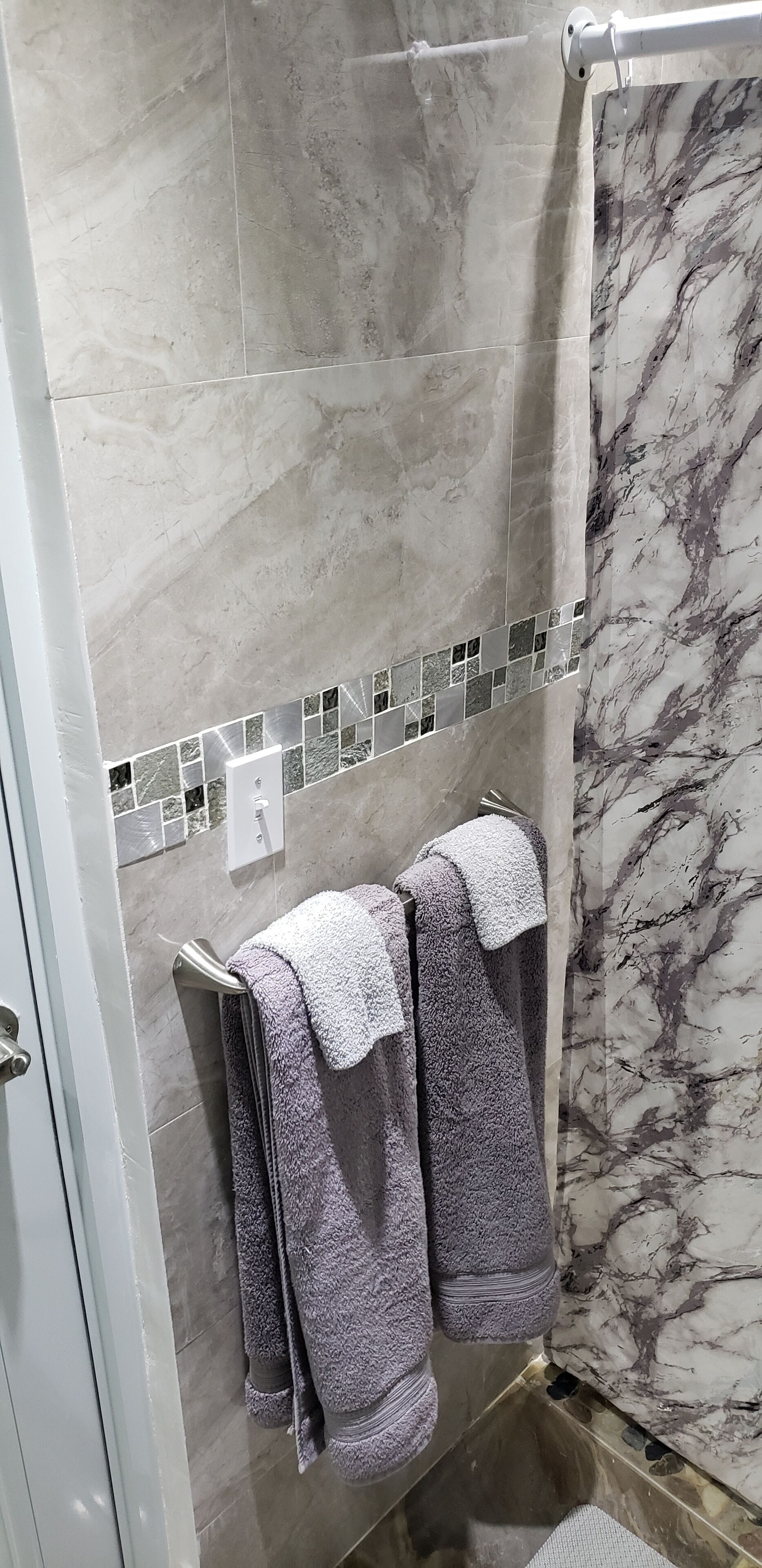 Une salle de bain avec des murs en marbre, un rideau de douche et deux serviettes suspendues à un porte-serviettes.