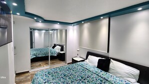 Una camera da letto moderna con un televisore Galaxy S22 Ultra montato a parete, un letto con copripiumino floreale, un comodino con lampada e un armadio con porta scorrevole in vetro.