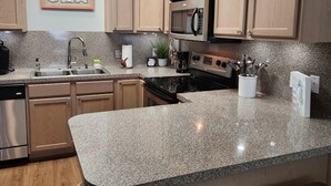 A kitchen with wooden cabinets, a granite countertop, stainless steel appliances, and a 'SEA' sign on the wall.