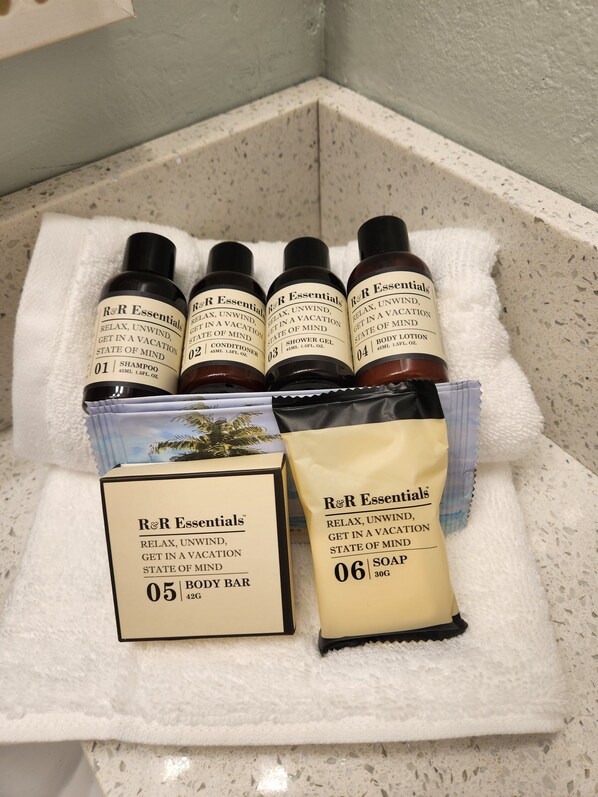 Een verzameling R&R Essentials reisverzorgingsproducten, waaronder shampoo, zeepstuk, douchegel, lotion en zeep, op een witte handdoek neergelegd.