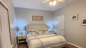 A bedroom with a bed, a ceiling fan, a nightstand, and a wall sign.