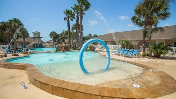 A pool area with a circular water feature, lounge chairs, and palm trees.