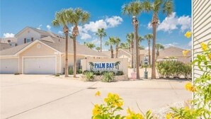 A residential area with a sign reading "PALM BAY VILLAGE" surrounded by palm trees and houses.