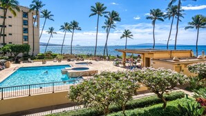 A hotel pool area with a view of the ocean, palm trees, and a building with multiple floors.