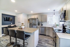 A modern kitchen with a central island, bar stools, stainless steel appliances, and a flat-screen TV mounted on the wall. - Port Clinton 4 Bdrm Luxury-2 blocks from beach (Port Clinton)