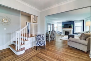 A spacious living room with hardwood flooring, a staircase, a dining area, and a fireplace.