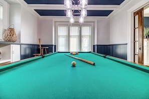 A pool table with a cue stick and a ball, a woven basket, and a chair.