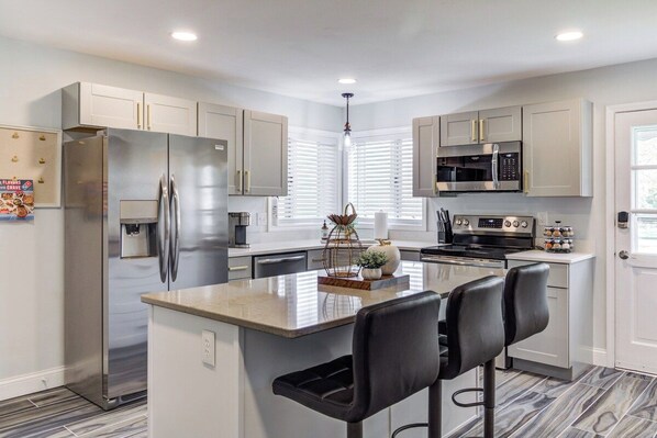 A modern kitchen with stainless steel appliances, a central island with bar stools, and a window with blinds.