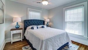 A bedroom with a tufted headboard, a large bed, two bedside tables with lamps, a ceiling fan, and a window with blinds. - Port Clinton 4 Bdrm Luxury-2 blocks from beach (Port Clinton)