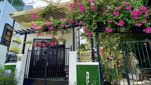 A gated entrance with a pergola covered in pink flowers, a signboard, and potted plants. - Ngo Family Apartment (Da Nang)