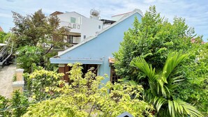 A residential area with a blue-roofed house, lush greenery, and a metal railing. - Ngo Family Apartment (Da Nang)