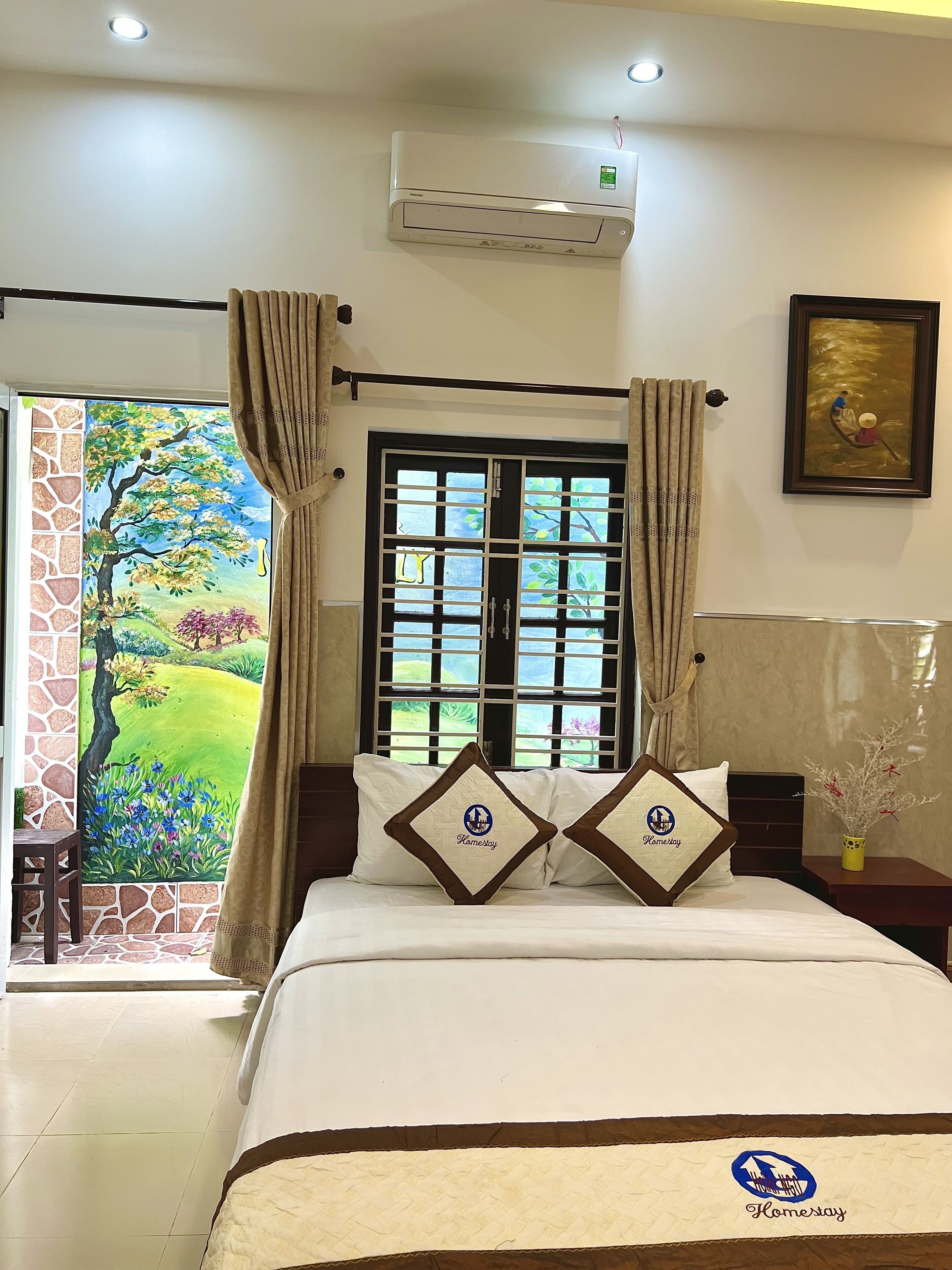 Habitación de hotel con cama, ventana con cortinas, aire acondicionado y un cuadro en la pared.