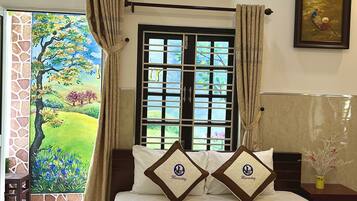 Habitación de hotel con cama, ventana con cortinas, aire acondicionado y un cuadro en la pared.