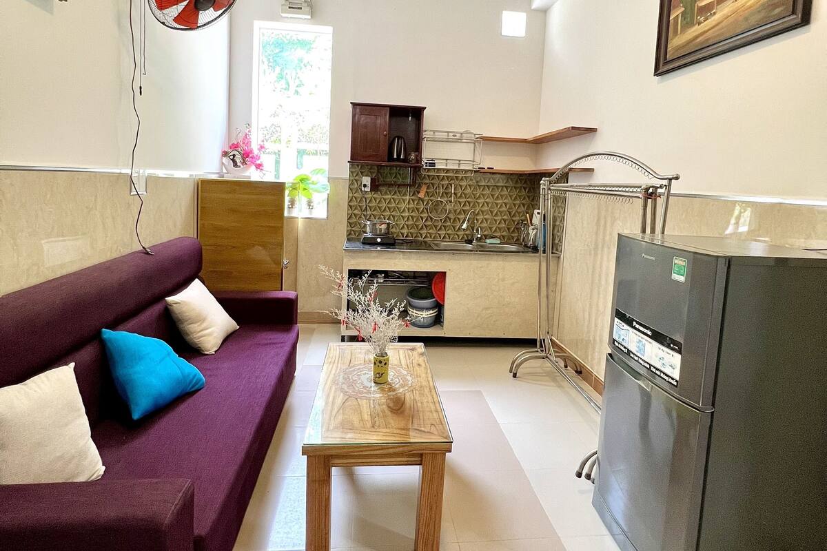 A compact living space with a sofa, a small wooden table, a refrigerator, and a kitchen area with a sink and cabinets.