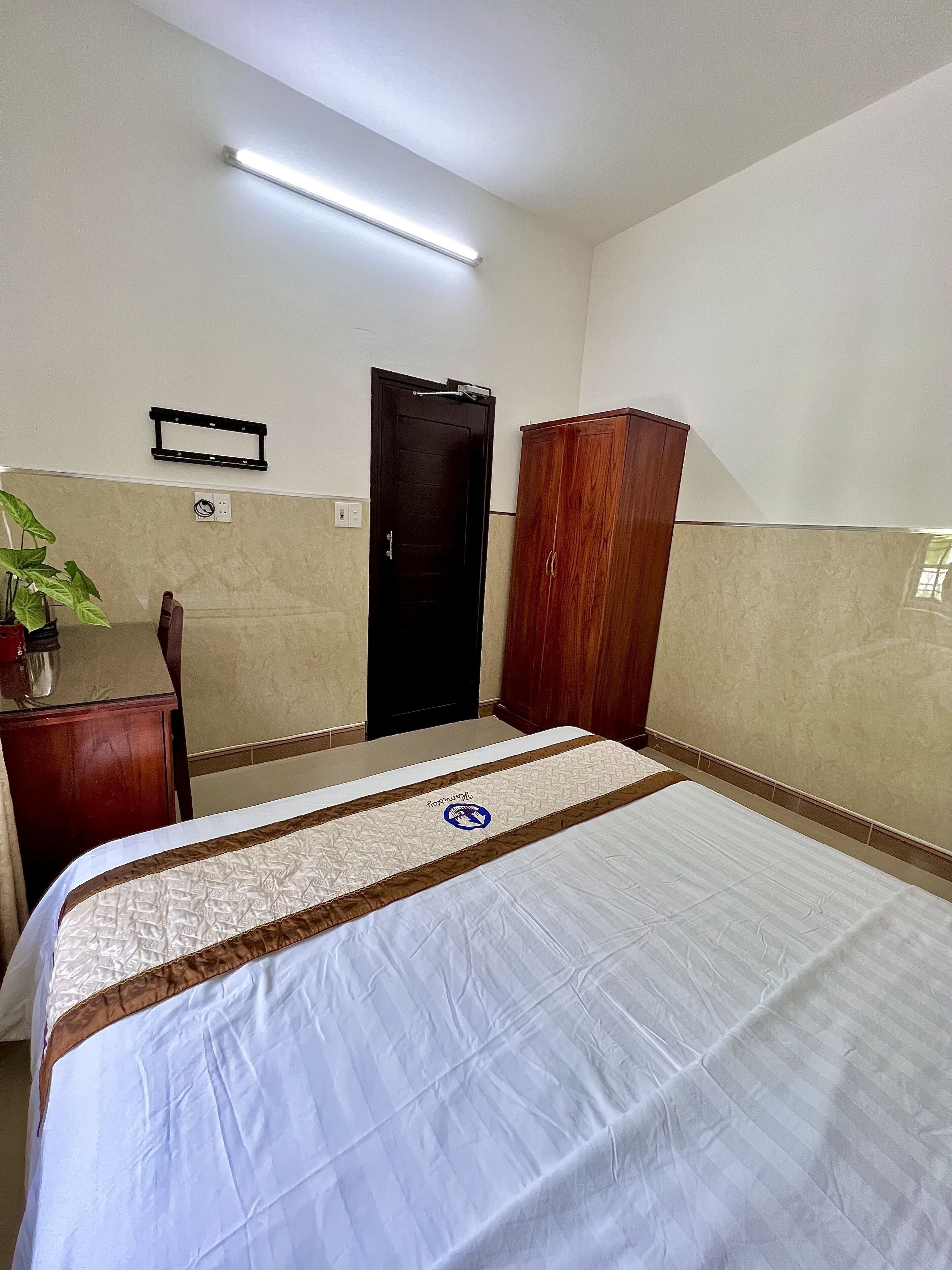 Una habitación de hotel con una cama, un armario de madera, un escritorio y una planta en maceta.