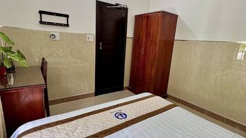 Una habitación de hotel con una cama, un armario de madera, un escritorio y una planta en maceta.