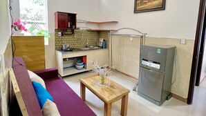 A compact living space with a sofa, a small table, a kitchenette, and a refrigerator. - Ngo Family Apartment (Da Nang)