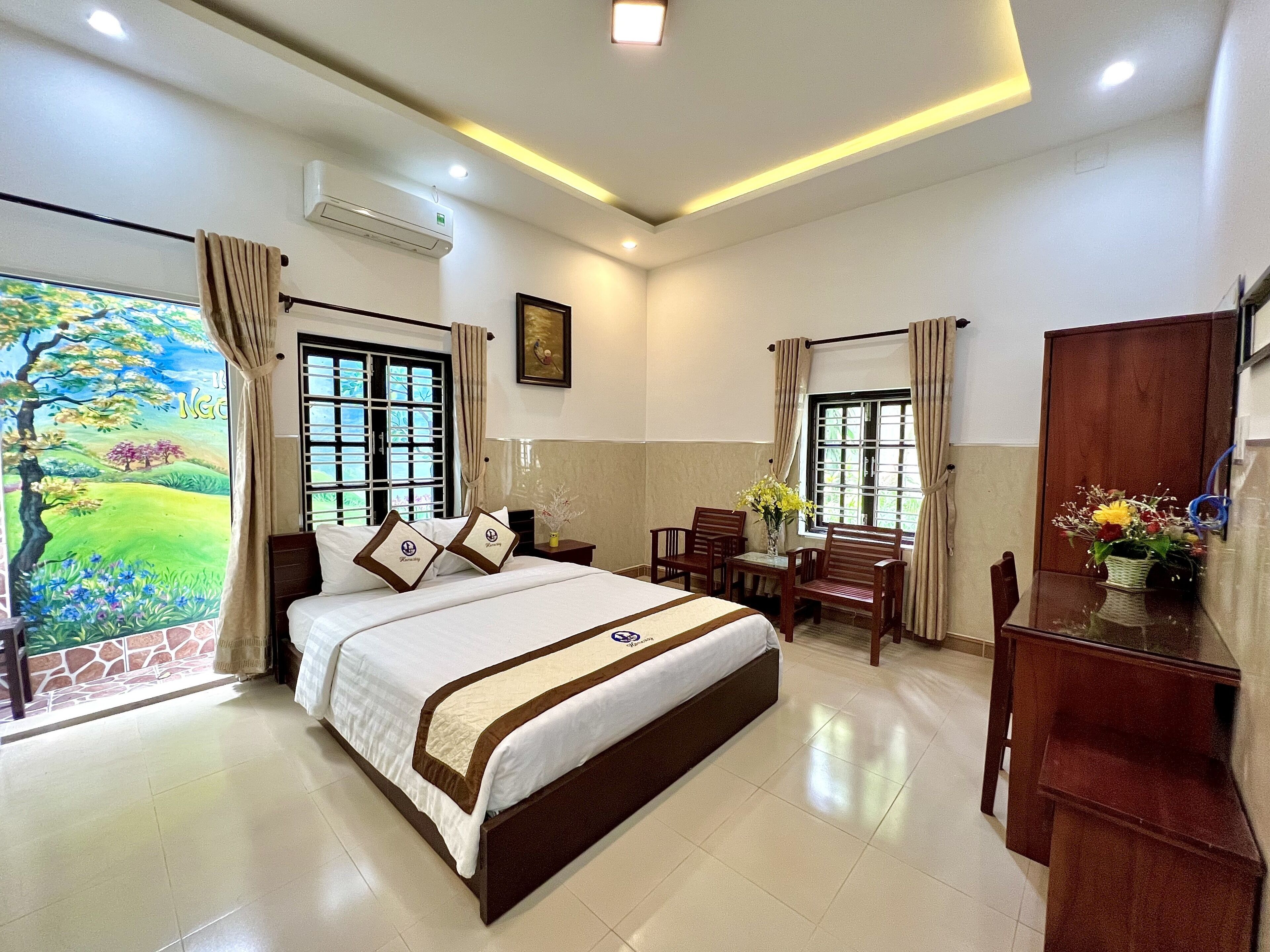 A hotel room with a large bed, a desk with chairs, a wooden cabinet, and a window with curtains.