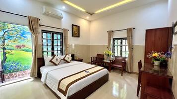 A hotel room with a large bed, a desk with chairs, a wooden cabinet, and a window with curtains.