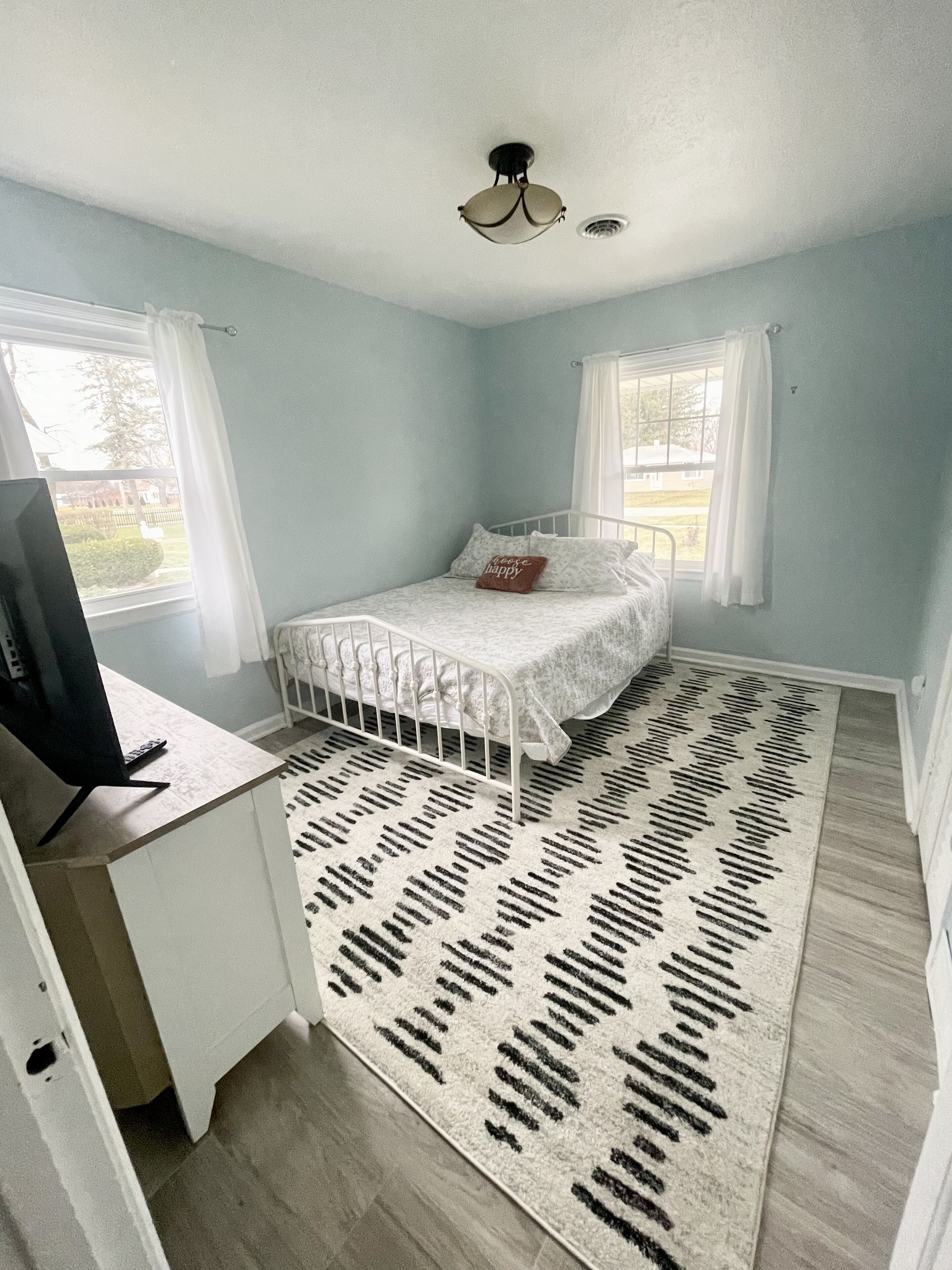Un dormitorio con una cama, un escritorio, una computadora y una alfombra estampada.