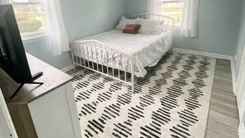 Un dormitorio con una cama, un escritorio, una computadora y una alfombra estampada.
