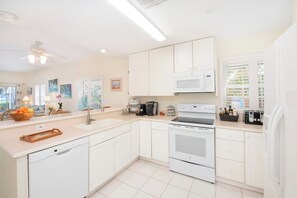 A modern kitchen with white cabinetry, a built-in oven, a microwave, and a coffee maker.