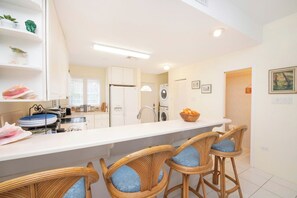 Une cuisine moderne avec des meubles blancs, un îlot central doté de tabourets de bar et un coin repas.