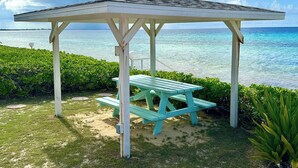Un jardín con techo a techo, una mesa de picnic y vegetación circundante, con vistas a un cuerpo de agua.