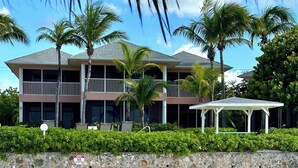 Un hotel frente a la playa con un muelle de madera que llega al agua, un área de estar techada y un edificio de dos pisos con balcones.