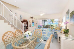 A living room with a sofa set, a dining table with chairs, a bookshelf, and a view of the outdoors.