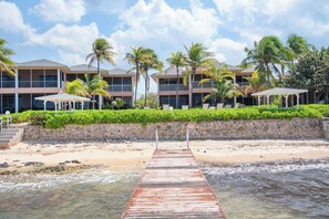 Une jetée en bois menant à un hôtel en bord de mer, doté de nombreux balcons et bordé de palmiers.