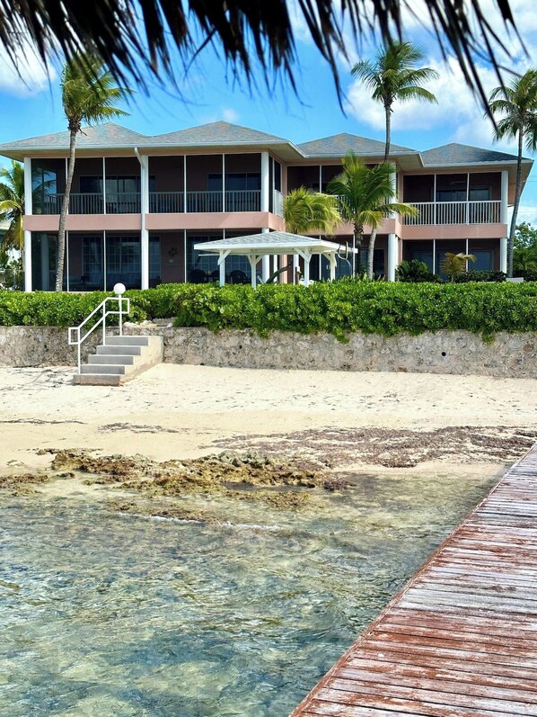 A beachfront property with a multi-story building, a covered patio, and a wooden walkway leading to the beach.