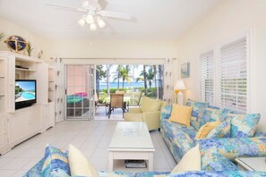 A living room with a television, a sofa, a coffee table, and a view of the outdoors. - Northern Lights 3 - 2BR/2.5BA Oceanfront Condo w/ Pool & Dock on Northside (North Side)