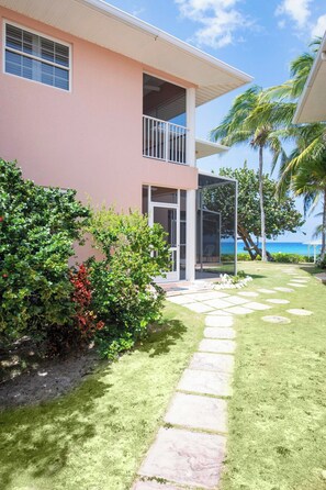 A two-story building with a balcony, a stone pathway leading to the entrance, and a view of the ocean.