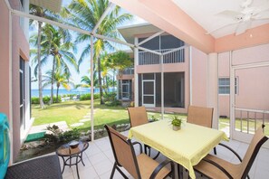 A balcony with a table and chairs, overlooking a lawn with palm trees and a view of the ocean.