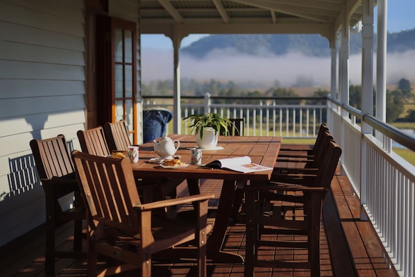 A wooden table with chairs on a covered porch, a potted plant, and a view of a misty landscape. - Cookes Road Cottage at Conondale (Conondale)