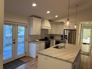 Une cuisine moderne avec des meubles blancs, un plan de travail en marbre, des appareils électroménagers en acier inoxydable et des luminaires suspendus.