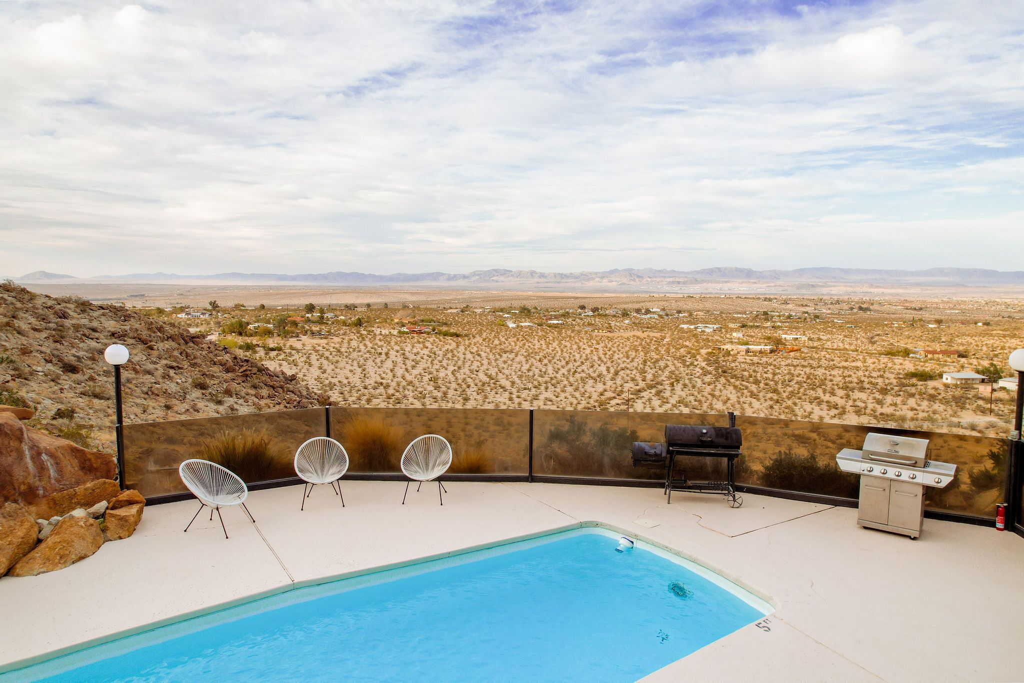 A pool area with a view of a desert landscape, including a barbecue setup and lounge chairs.