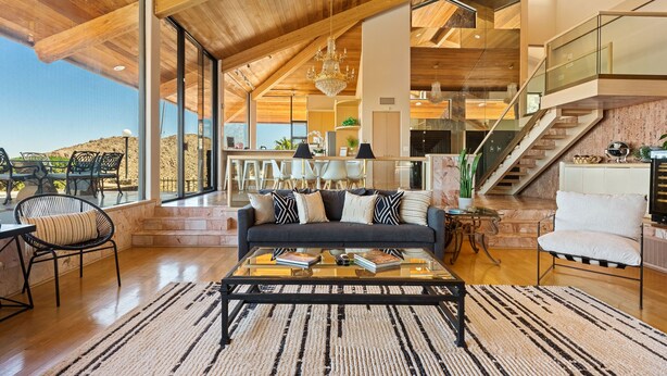 Un amplio salón con techos altos, un sofá grande, una mesa de centro y una escalera que sube a un nivel superior.