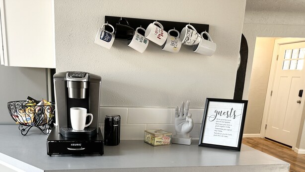 Eine Küchenarbeitsplatte mit Kaffeemaschine, Tassen und einem gerahmten Schild.