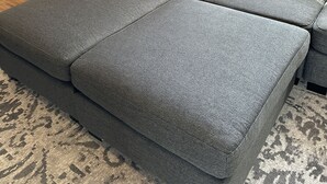Ein modulares Sofa mit grauem Stoff und einem einzelnen hellgrauen Kissen.
