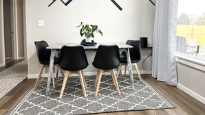 Ein Essbereich mit Tisch, Stühlen, einer Topfpflanze und einem geometrischen Wandmuster.