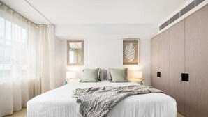 A bedroom with a large bed, two bedside lamps, a mirror, a framed leaf artwork, and a wardrobe. - Bondi Breeze (Bondi)