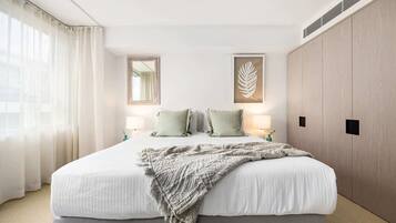 Une chambre à coucher avec un grand lit, deux lampes de chevet, un miroir, une œuvre d’art représentant une feuille encadrée et une armoire.