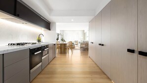 A modern kitchen with a central island, built-in appliances, and a dining area with a wooden table and chairs. - Bondi Breeze (Bondi)