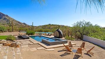 Un área de piscina con sillones de descanso, un jacuzzi y vistas a un paisaje montañoso.