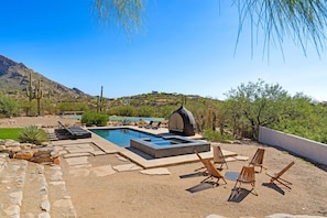 A pool area with lounge chairs, a hot tub, and a view of a mountainous landscape.