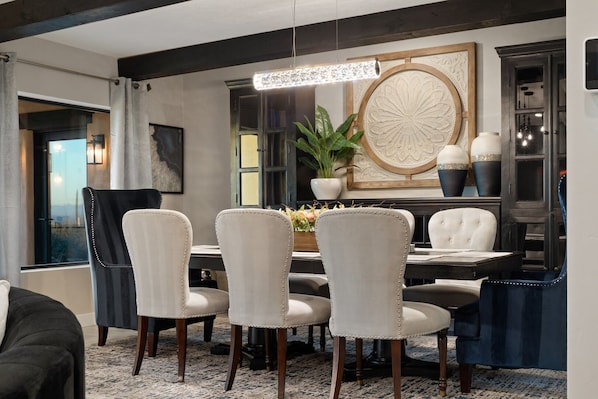 A dining area with a round table, six chairs, a chandelier, a potted plant, and a decorative wall piece. - Catalina Clubhouse | Luxury Retreat in Tucson | Fieldtrip (Tucson)