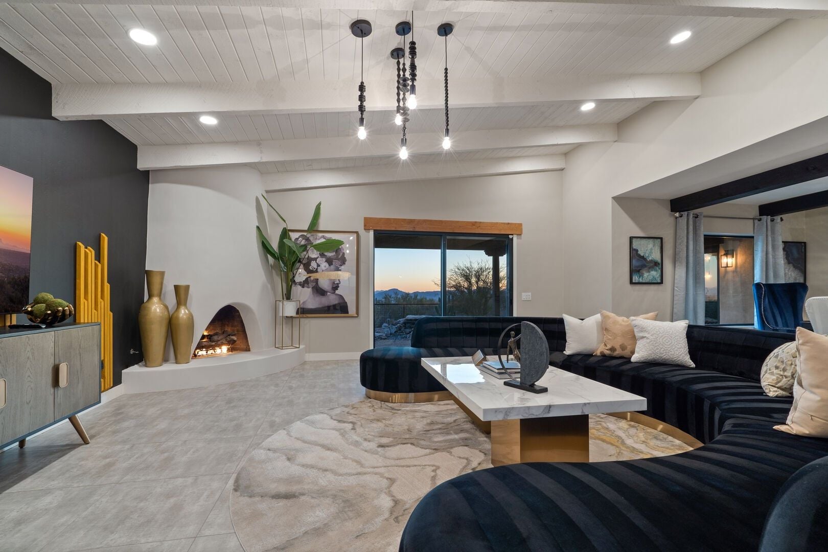 A modern living room with a fireplace, a sofa set, a marble coffee table, and a large window with a view.